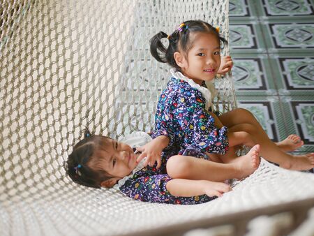 Happy little Asian baby girls, sisters, enjoys being together on a hammock - sibling relationshipの写真素材