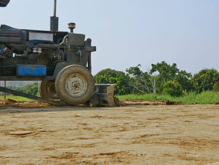 A tractor mounted with front grader is preparing an entrance ramp connected between higher and lower...
