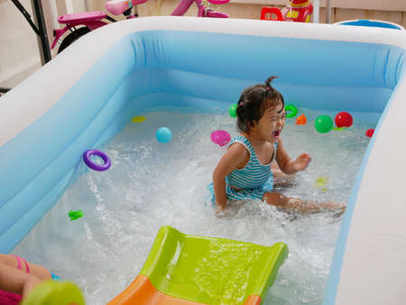 Little baby girl enjoys / having fun playing water in a pool at home