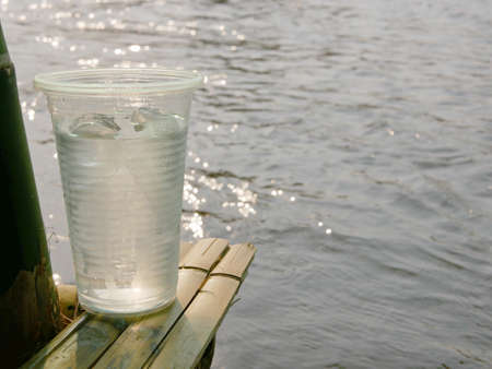 A cup of iced cold refreshing drinking water on a bamboo terrace with flowing river and reflection of the evening sky in the backgroundの写真素材