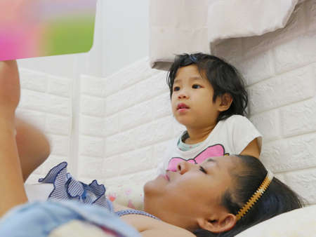 Little Asian baby girl, 3 years old, enjoys listening to her mother reading a bedtime story tale from a bookの写真素材