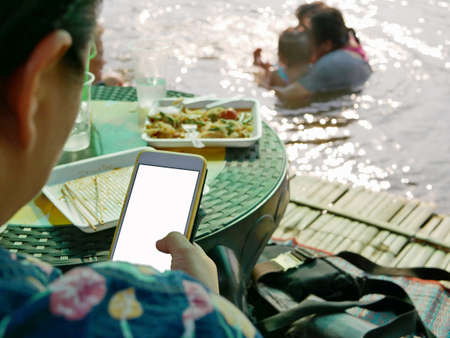 A smartphone in a woman's hand sitting and relaxing in a small bamboo hut by a river - being away...