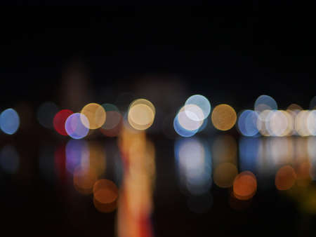 Bokeh of colorful lights on the bank of a river and their reflection, during night timeの写真素材