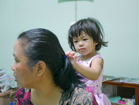 Little baby girl, 2 years old, enjoys playing / pretending to do her auntie's hairs at homeの写真素材
