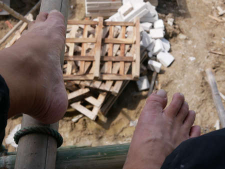 Closeup of bare feet of a worker above the ground on bamboo scaffolds that are installed around the...