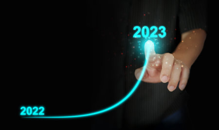 A man's finger draws an upwards curved line from 2022 to 2023. New Year, Christmas, start-up, new business, setting a personal goalの写真素材