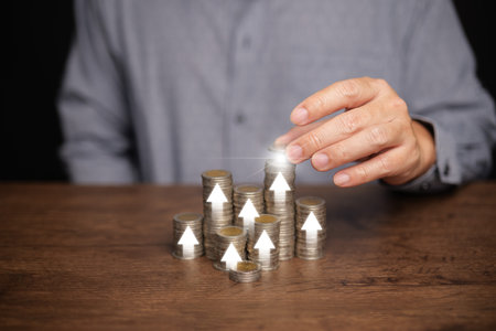 Saving money, investing, and financial planning. A man's hand placing a coin on a stack, with rising...