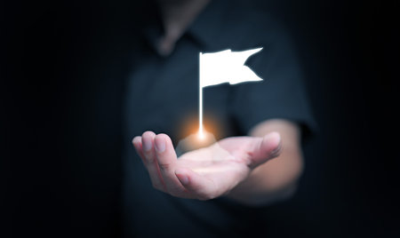 Glowing flag rising above businessmanâs hand, representing success, goal achievement, triumph, and determination. Ideal for business strategy, leadership, recognition, and milestone concepts.の写真素材