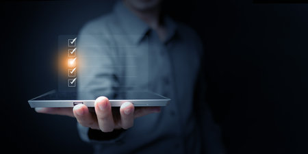 Hand holding tablet with checklist interface, illustrating digital business planning, corporate...