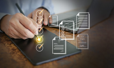 Hand writing checklist on digital tablet with laptop, illustrating project management, quality...