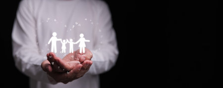 Hands holding family icon with hearts on dark background. Families love, mental health, emotional support, insurance protection, budgeting awareness, foster care, homeschool, and wellbeingの写真素材