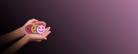 Hands holding three emotion face symbols sad, neutral, and happy on dark background representing mental health awareness, mood change, emotional balance, and psychological wellbeing,の写真素材