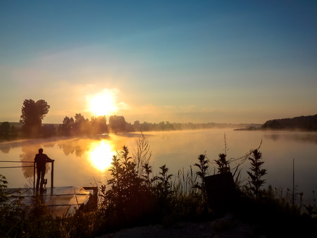dawn on the lake the silhouette of the man on the bridge an unforgettable landscapeの写真素材
