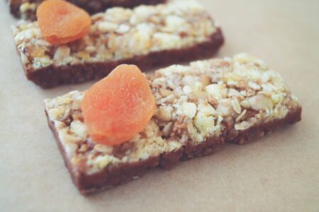 Food Dessert Bar with muesli cereals and chocolate with dried apricots on brown background of parchment paper isolateの写真素材