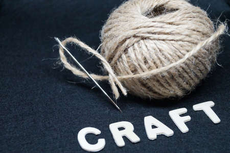 ball of natural coarse threads with a needle and the inscription wooden craft letters on a black backgroundの写真素材