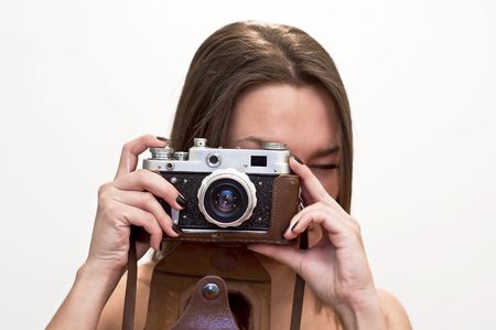 Young woman looks at an old film camera. Studio shot on white background. 