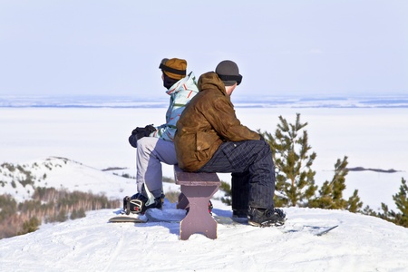 Two snowboarders resting on top of mountain against the backdrop of a beautiful winter landscape  Back to back の写真素材