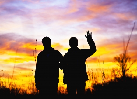 Hello. Two men stand in the background of a beautiful sunset and waving his hand in greeting Hello. Silhouettes in the contre. Special light.の写真素材