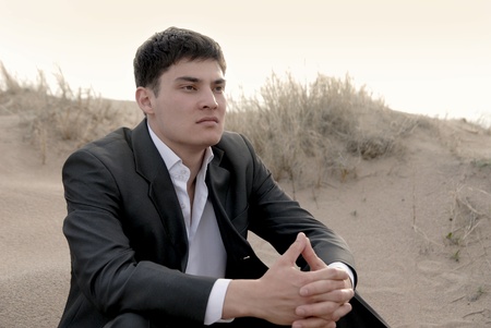 young guy (businessman) sits in the desert and think hard about somethingの写真素材
