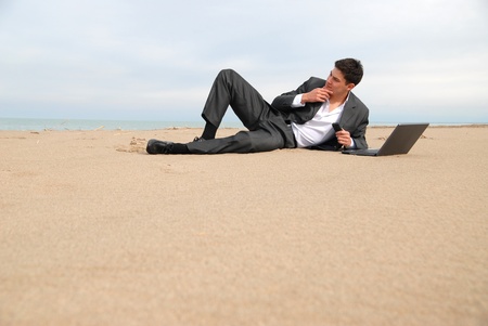 A young businessman lying on the beach in front of a laptop, he thought.の写真素材