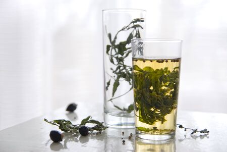 Glass cup with tea from the leaves and stems of mint on a light background. Around the dry stalks of mint, rose, glass beaker with dried mint.の写真素材