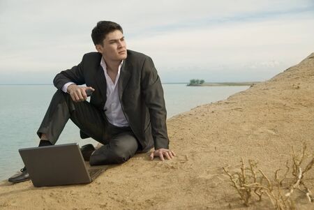 the young guy a businessman on the beach with a laptop looks into the distanceの写真素材