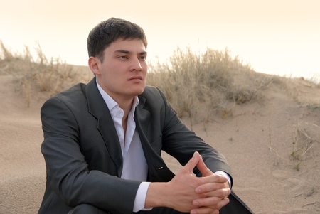 young guy (businessman) sits in the desert and think hard about somethingの写真素材