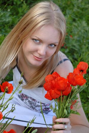 Young blond girl with a bouquet of poppies in the poppy field. The girl smiles.の写真素材