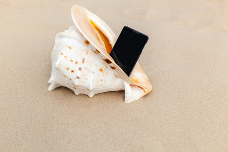 smartphone and a sea shell on the sand near the seaの写真素材