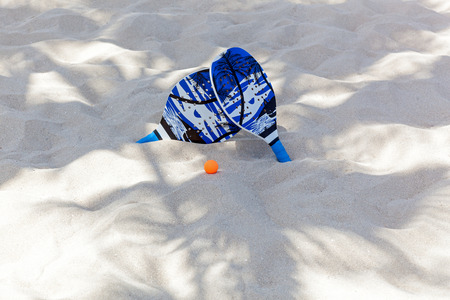 beach tennis,In palms shadow there are rackets and a ball on the sandの写真素材