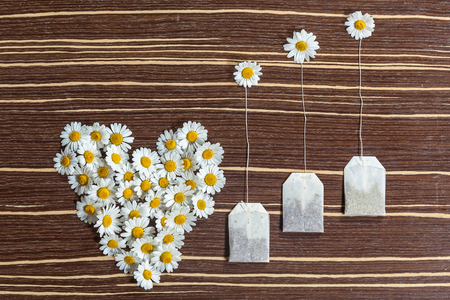 Tea and flower composition. The original tea and flower composition on a wooden table. There is a heart of the camomiles, and are tea bags and a cup on a saucer with a spoon, and raisins in the syrup.の写真素材