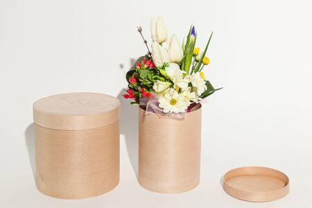 Different beautiful flowers in the basket, round beige box and handmade eggs close up on the white backgroundの写真素材