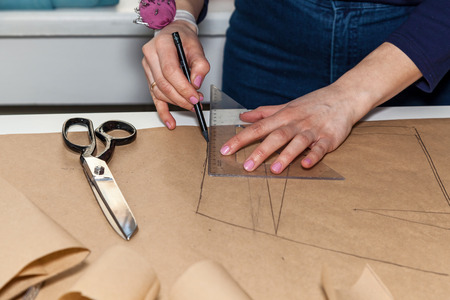 Seamstress is cutting drawing for a dress with scissors. Style and design development and creating garment, clothes sew and repair service, seamstress at work conceptの写真素材