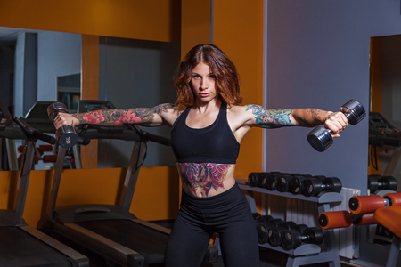 girl doing exercises with dumbbells.girl with tattoos on fitness demonstrates a beautiful body with muscles.Various sports equipment and fitness equipment for sports and fitnessの写真素材