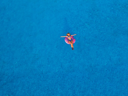 Aerial top view of beautiful girl in swimming pool from above, relax swim on inflatable ring donut and has fun in water on family vacationの写真素材