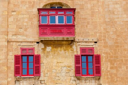 Malta architecture, facade of a house with red wooden windows and a balcony on the island of Malta