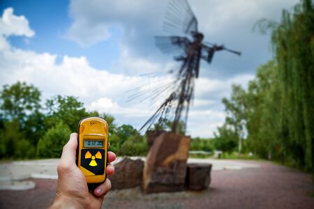 Dosimeter in hands with a level of radioactivity near the monument in memory of the Chernobyl accident. Chernobyl disaster story. Lost place in Ukraine, USSRの写真素材