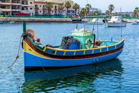A colorful luzzu near the shore of a fishing village on a sunny day, Malta. The fishing boat in blue and yellow colors is located in the harbor.の写真素材