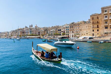 An amazing sea view with traditional Maltese boats on the background of old buildings on a summer sunny day in Malta, Europe.の写真素材