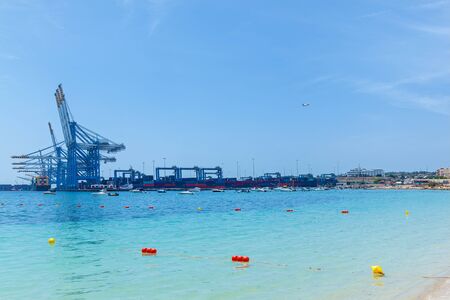 An amazing view of an industrial port with many cargo ships near construction cranes on the sea on the background of a blue sky in Malta.の写真素材