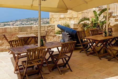An outdoor cafe terrace with tables and chairs with a view of a coastal city on a sunny day.の写真素材