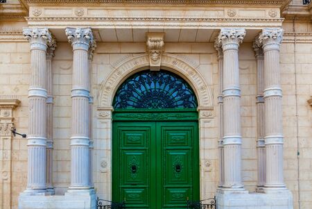 The facade of a historic building with big stone columns and decorative elements. The green front...
