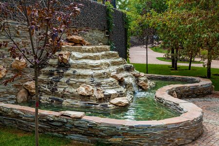An outdoor stone waterfall located in a green area of the park on a sunny day.の写真素材