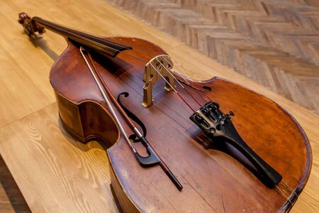 An old broken double bass lying on a wooden table on the background of a wall.の写真素材