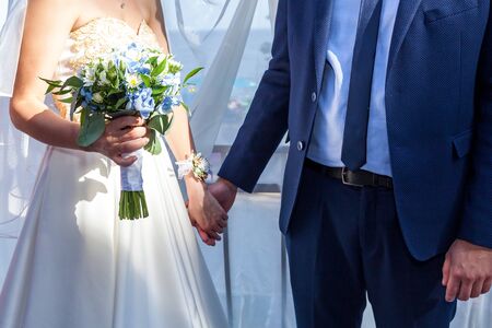 A bride is holding a wedding bouquet with roses in hands.