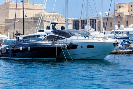 White and black modern motor yachts are moored in port on the cityscape background.の写真素材