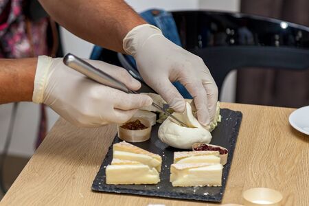 A woman is cutting pieces of cheese with a knife on a yellow plate for presentation. Close-up view...