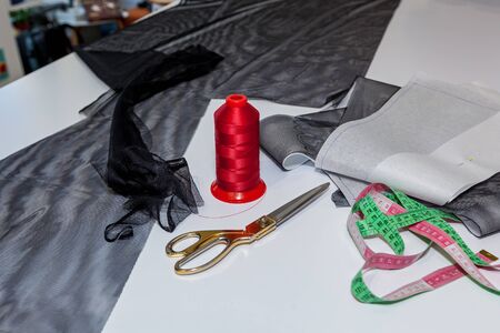 Threads, scissors, and fabrics laying on the wooden white table.
