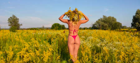 A young, attractive girl in a swimsuit, and with a bouquet of flowers on her head, posing in a field of flowers against the blue sky.の写真素材
