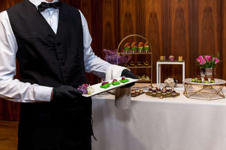 Waiter wearing black gloves carries snacks at a holiday event, party or wedding reception. Catering,...